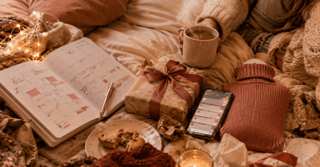 Gemütliche Winterszene mit überfülltem Kalender, Geschenk, Kaffeetasse, Handy, Wärmflasche und Lichterkette als Symbol für Weihnachtsstress und zu viele Dezember-Aufgaben. 